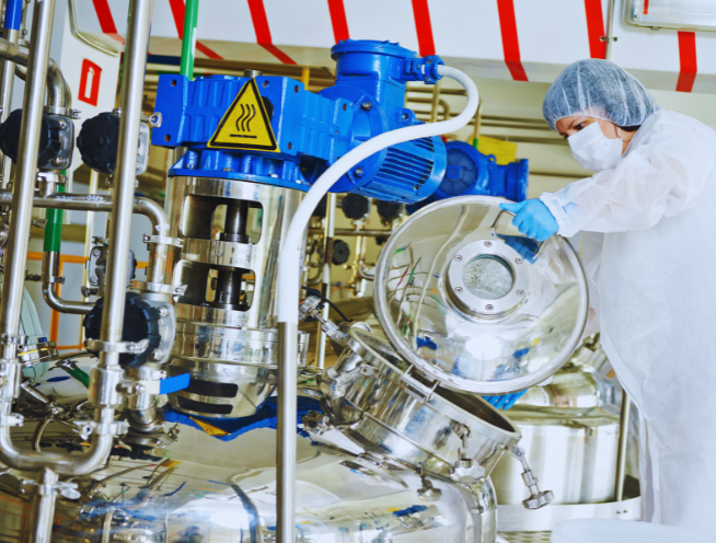 Technician working at a stainless steel reactor vessel in a pharmaceutical manufacturing facility